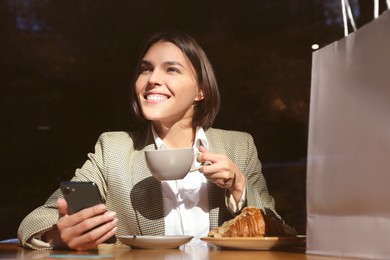 Special Promotion. Happy young woman with cup of drink using smartphone at table in cafe