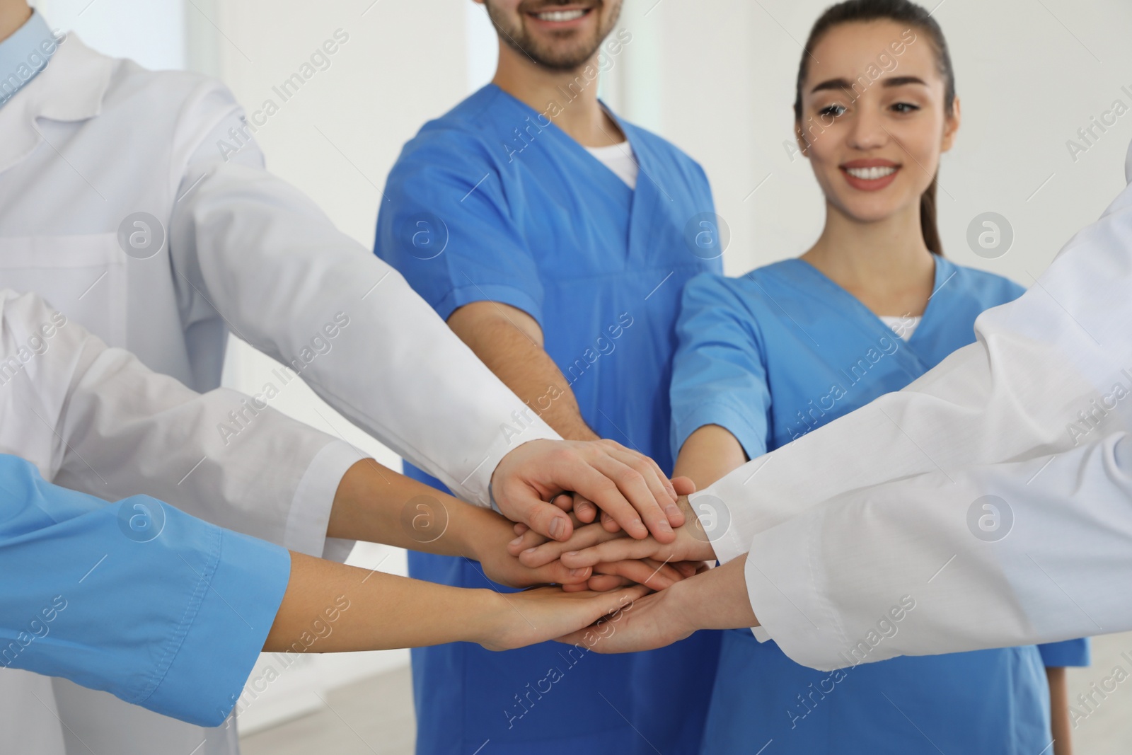 Photo of Team of medical workers holding hands together indoors. Unity concept