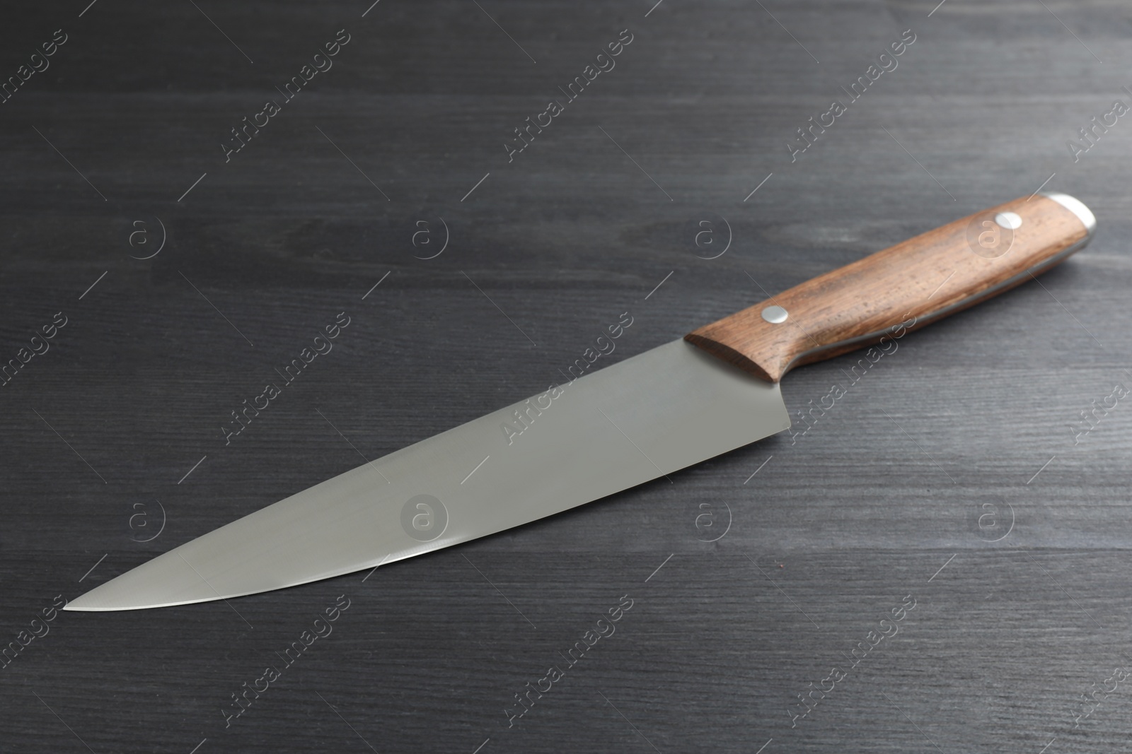 Photo of One sharp knife on black wooden table, closeup