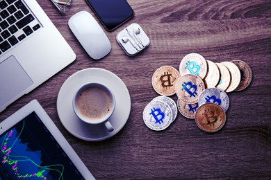 Bitcoins, cup of coffee and different gadgets on wooden table, flat lay