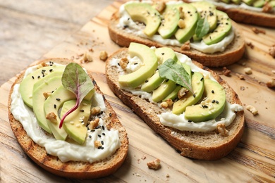 Photo of Delicious bruschettas with avocado served on wooden board, closeup