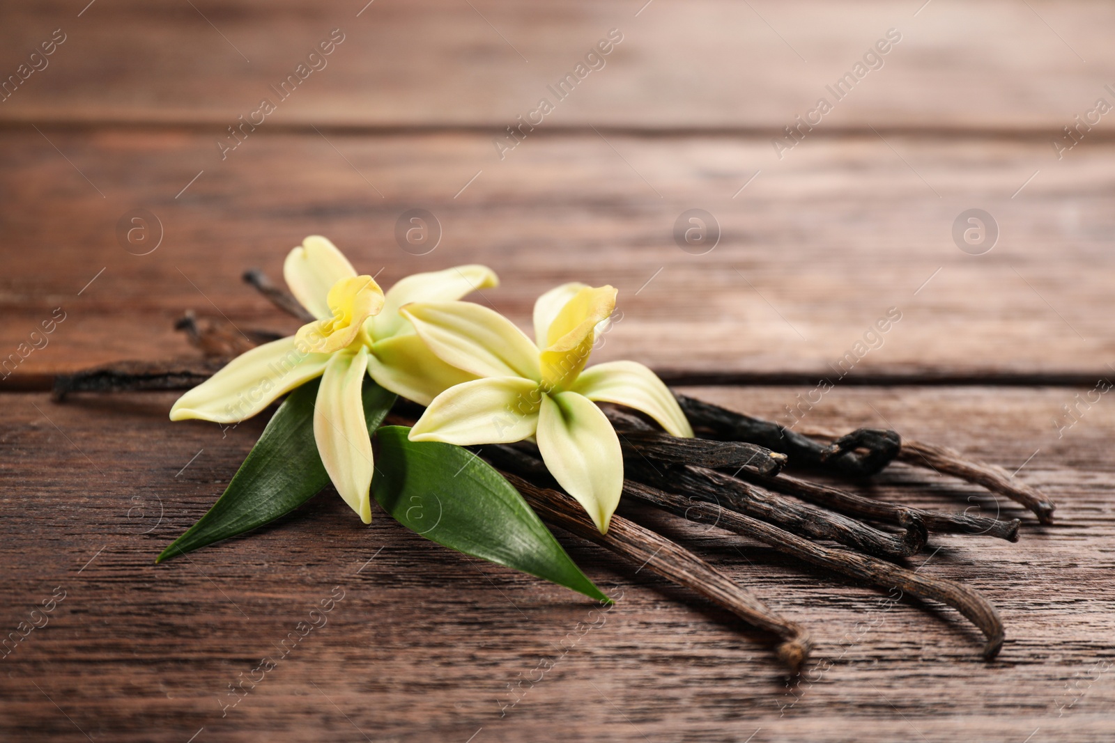 Photo of Beautiful vanilla flowers and sticks on wooden table, closeup