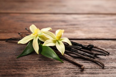 Beautiful vanilla flowers and sticks on wooden table, closeup