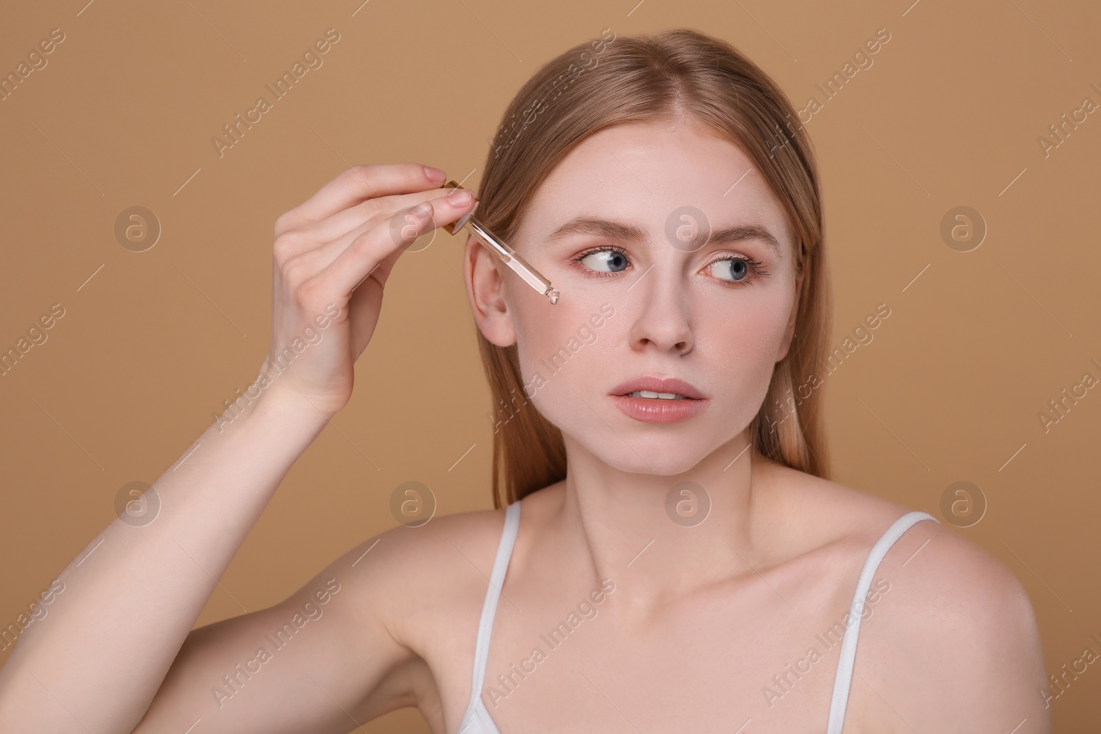 Photo of Woman applying essential oil onto face on light brown background