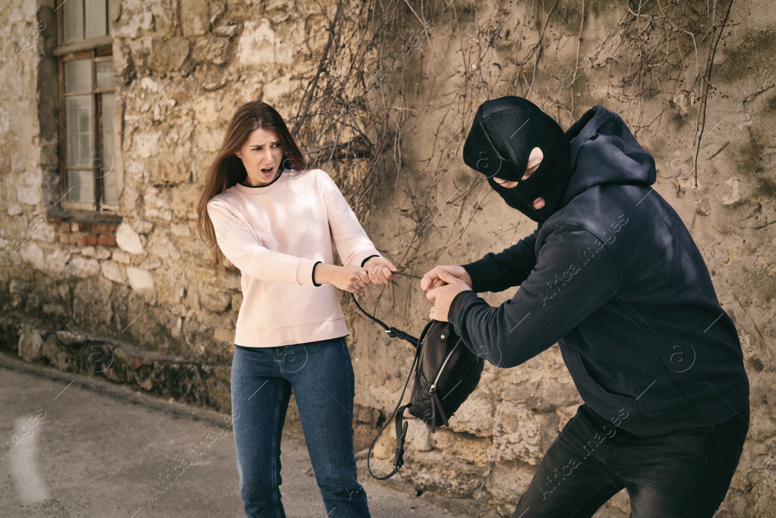 Photo of Masked man trying to steal woman's backpack outdoors. Criminal offence