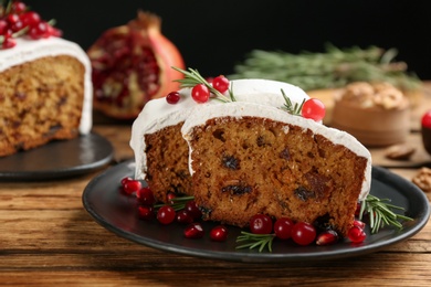 Traditional classic Christmas cake decorated with cranberries, pomegranate seeds and rosemary on wooden table
