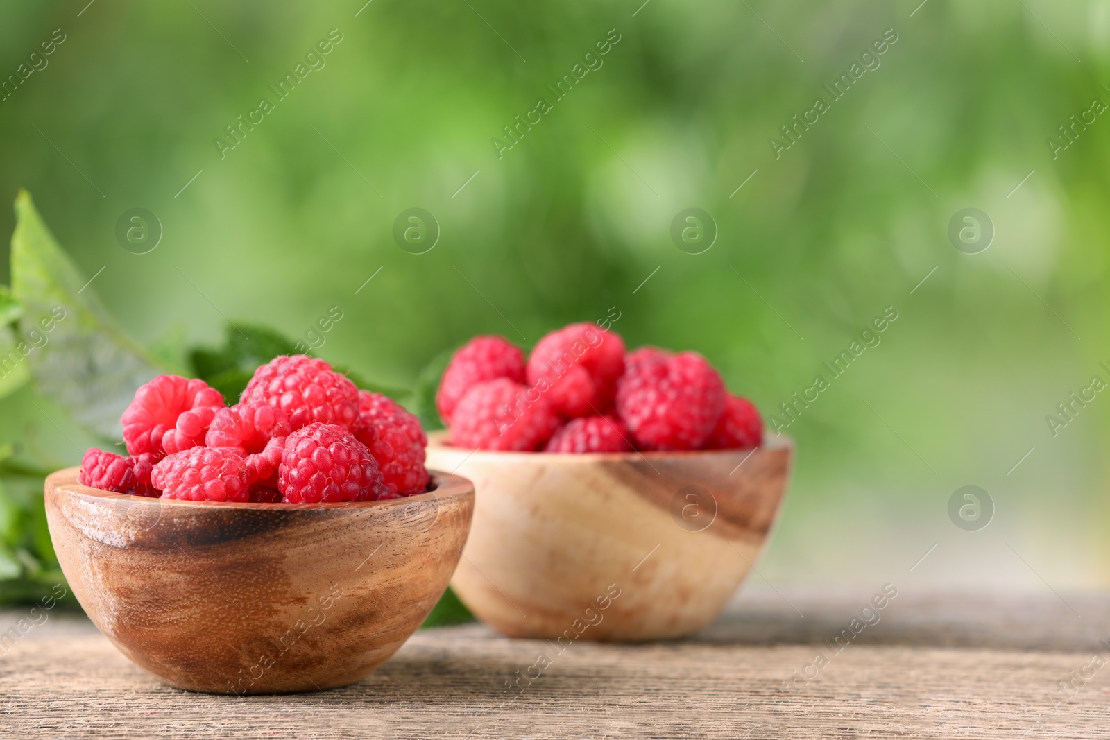 Photo of Tasty ripe raspberries in bowl on wooden table outdoors. Space for text