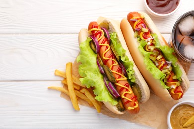 Photo of Delicious hot dogs with lettuce, onion and pickle served on white wooden table, flat lay. Space for text