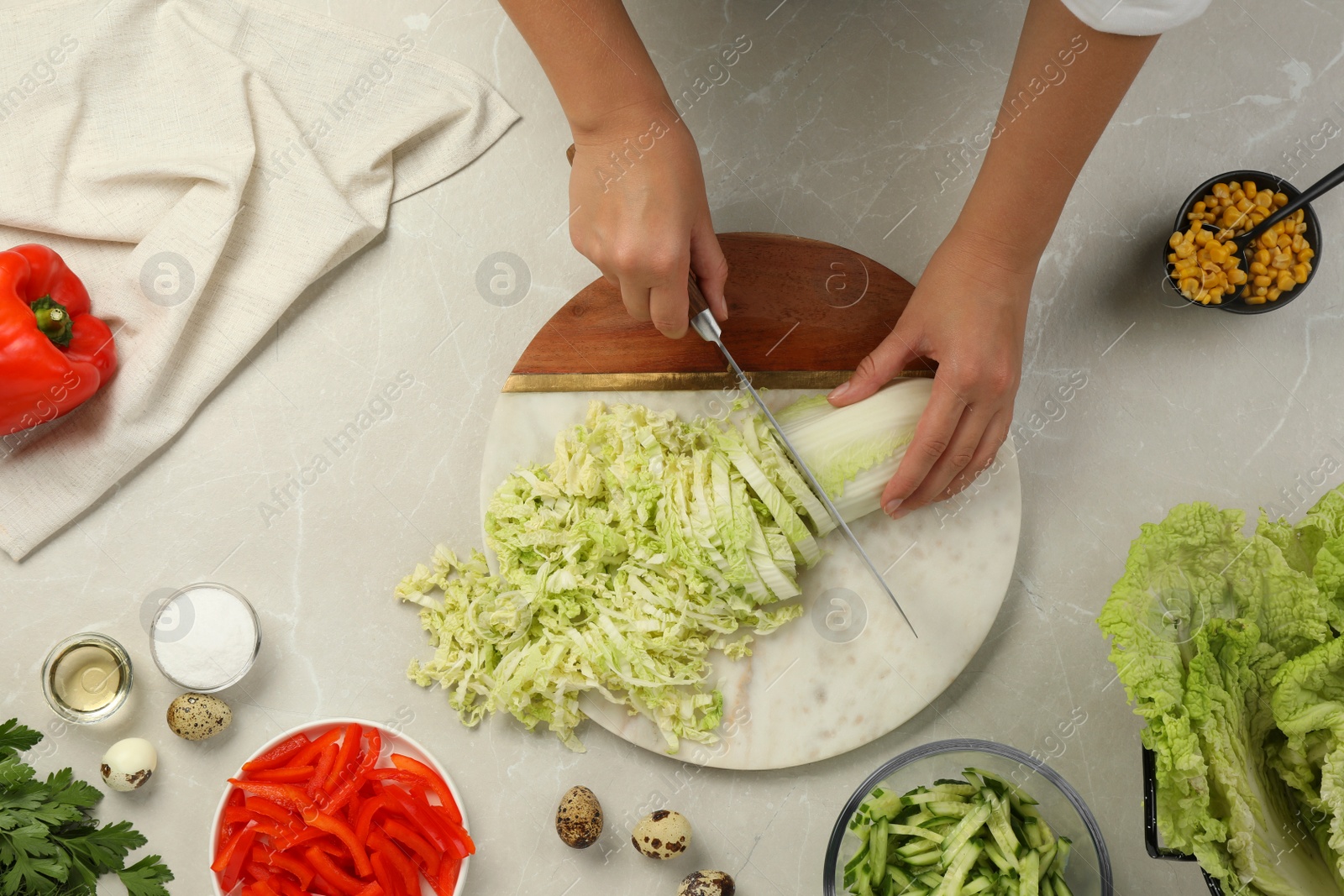 Photo of Woman cutting fresh Chinese cabbage at light grey table, top view