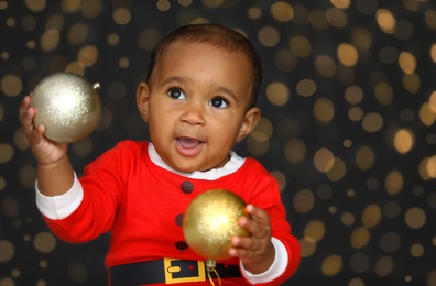 Cute little African American baby with Christmas balls and blurred lights on dark background