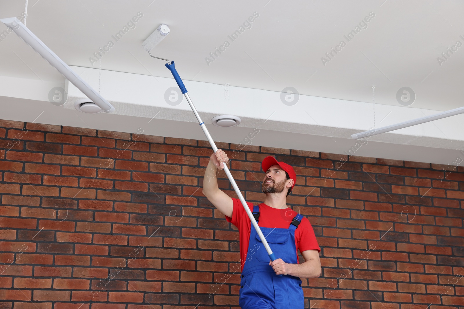 Photo of Handyman painting ceiling with roller in room