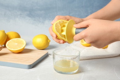 Photo of Woman squeezing lemon juice with reamer into glass on table