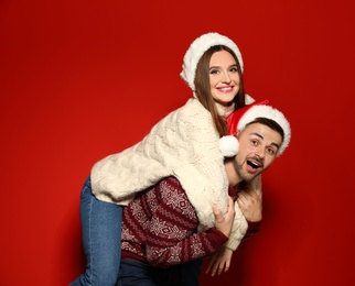 Couple wearing Christmas sweaters and Santa hats on red background