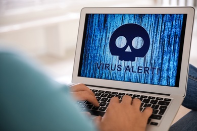 Photo of Man using laptop with warning about virus attack on screen at home, closeup