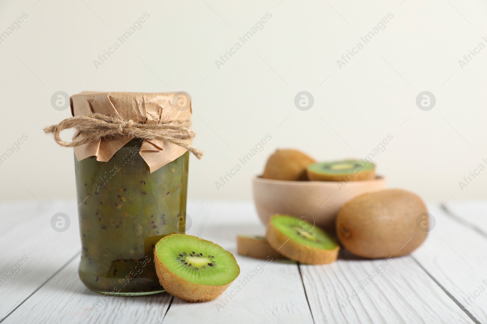 Photo of Jar of delicious kiwi jam and fresh fruits on white wooden table, space for text