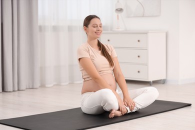 Pregnant woman doing exercises on yoga mat at home