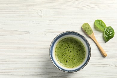 Photo of Cup of fresh matcha tea, green powder and leaves on white wooden table, flat lay. Space for text