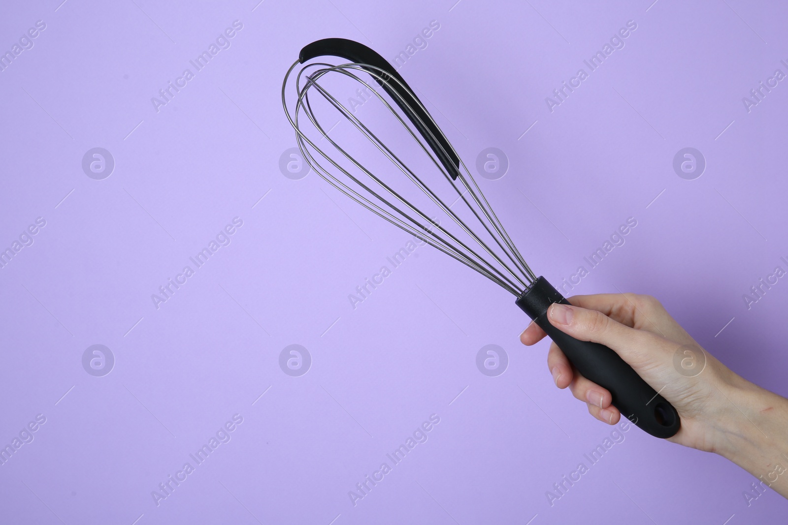 Photo of Woman holding metal whisk on lilac background, closeup. Space for text