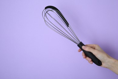 Woman holding metal whisk on lilac background, closeup. Space for text