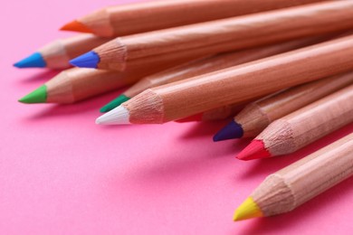 Photo of Many colorful pastel pencils on pink background, closeup. Drawing supplies