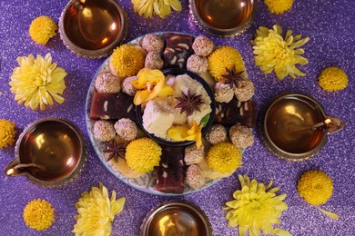 Photo of Diwali celebration. Flat lay composition with diya lamps and tasty Indian sweets on shiny violet table
