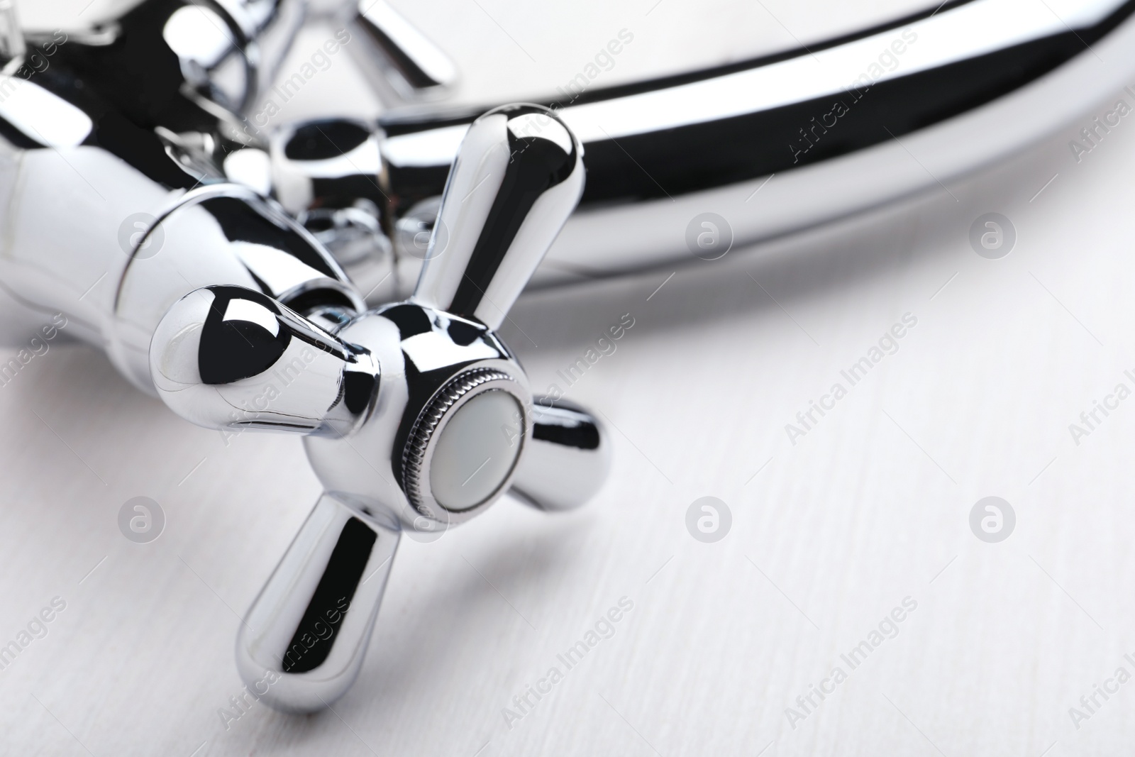 Photo of Double handle water tap on white wooden table, closeup