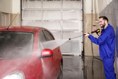 Worker cleaning automobile with high pressure water jet at car wash