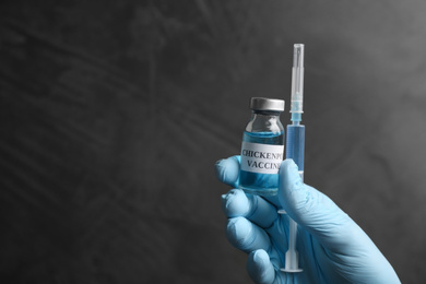 Photo of Closeup view of doctor holding chickenpox vaccine and syringe on grey background, space for text. Varicella virus prevention