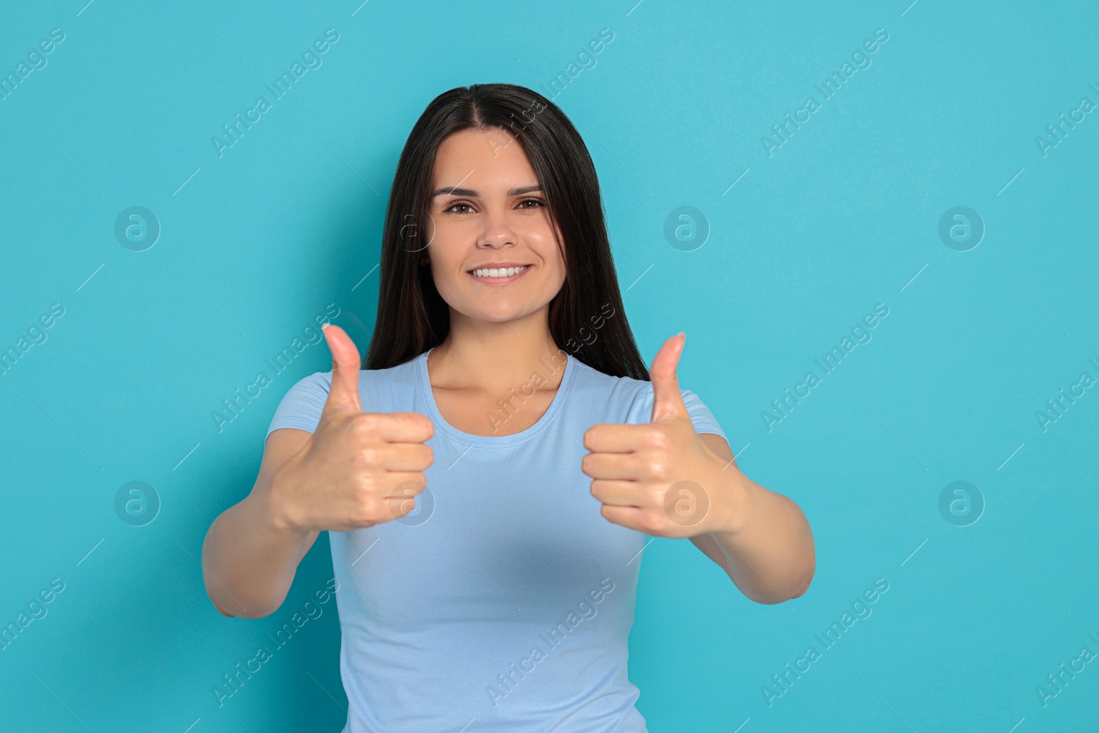 Photo of Young woman showing thumbs up on light blue background