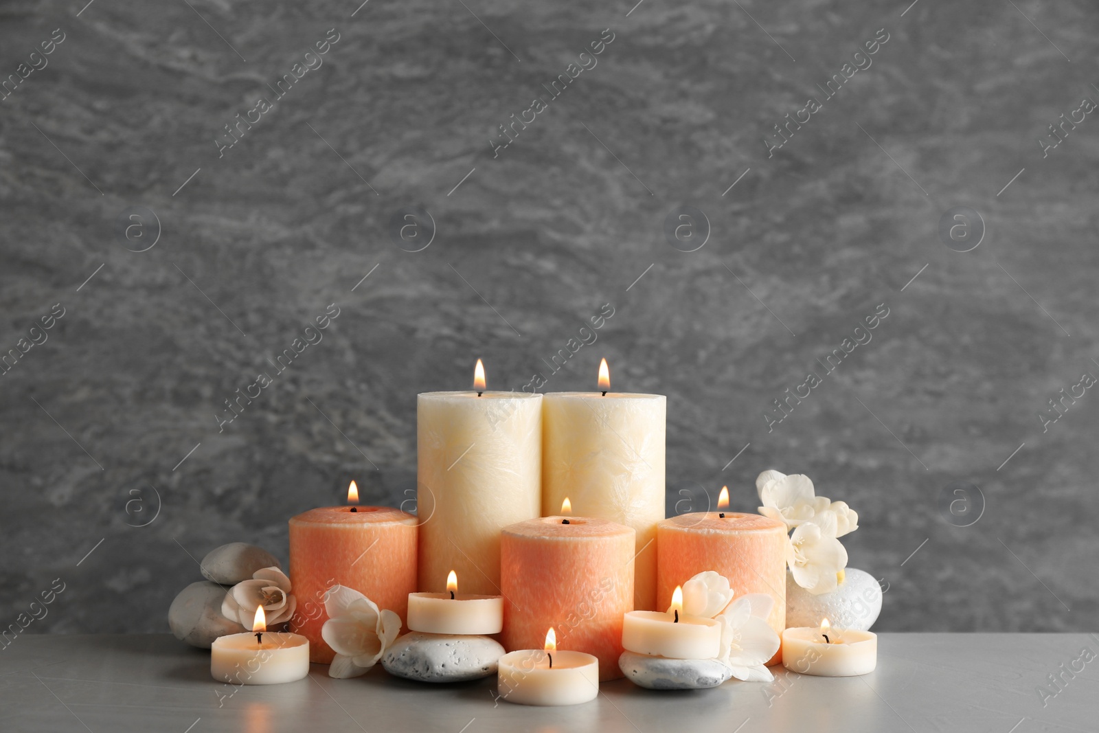 Photo of Beautiful composition with candles, flowers and stones on table against grey background. Space for text