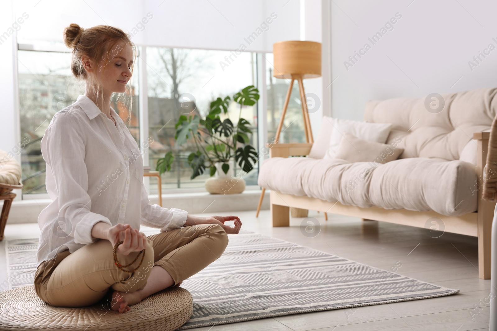 Photo of Woman meditating on wicker mat at home. Space for text