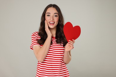 Beautiful young woman with paper heart on grey background