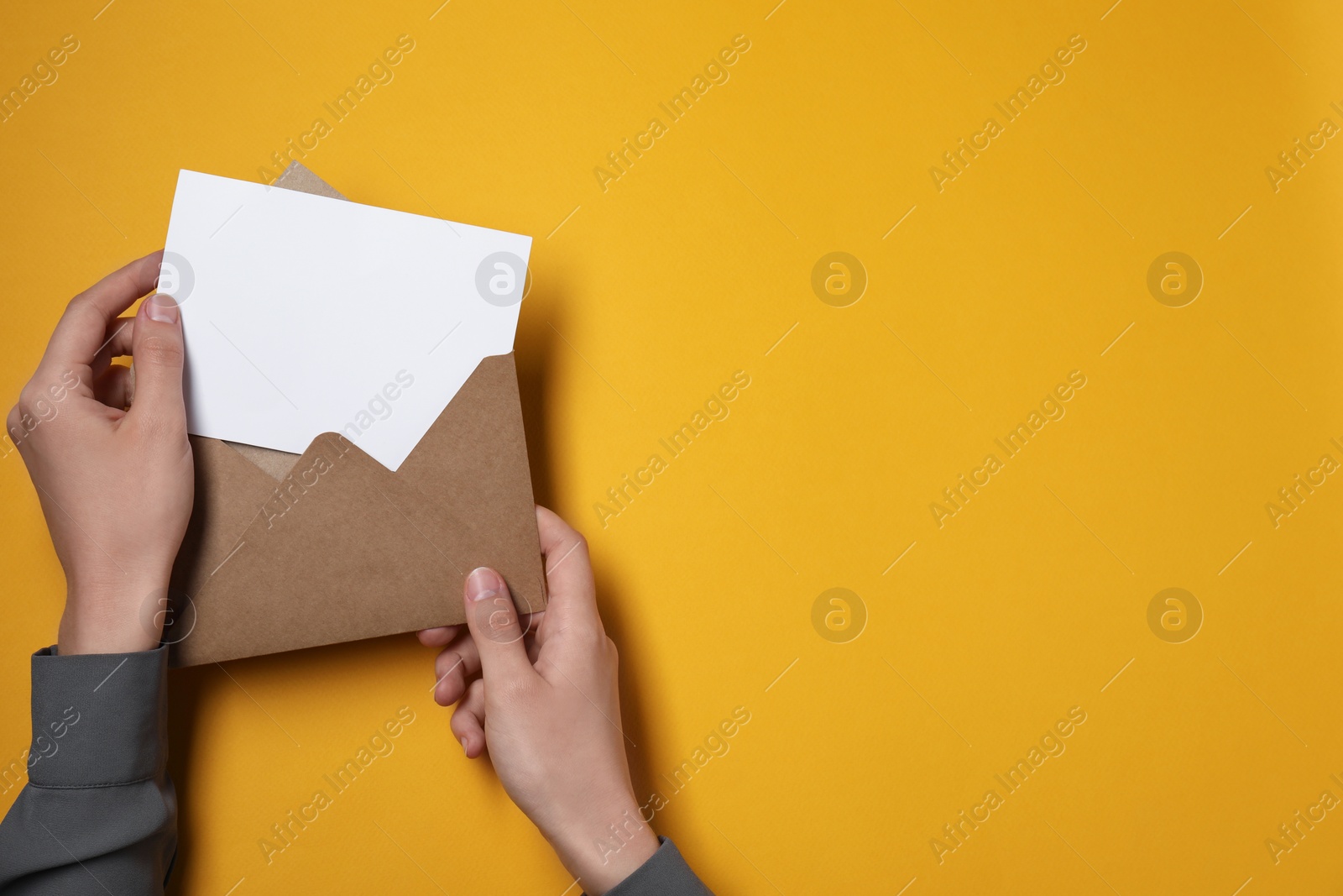 Photo of Woman taking card out of letter envelope at orange table, top view. Space for text