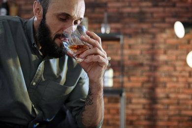 Photo of Handsome man holding glass of whiskey indoors. Space for text