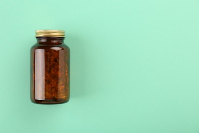 Bottle with vitamin capsules on turquoise background, top view. Space for text