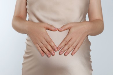Photo of Pregnant woman making heart with her hands on light grey background, closeup