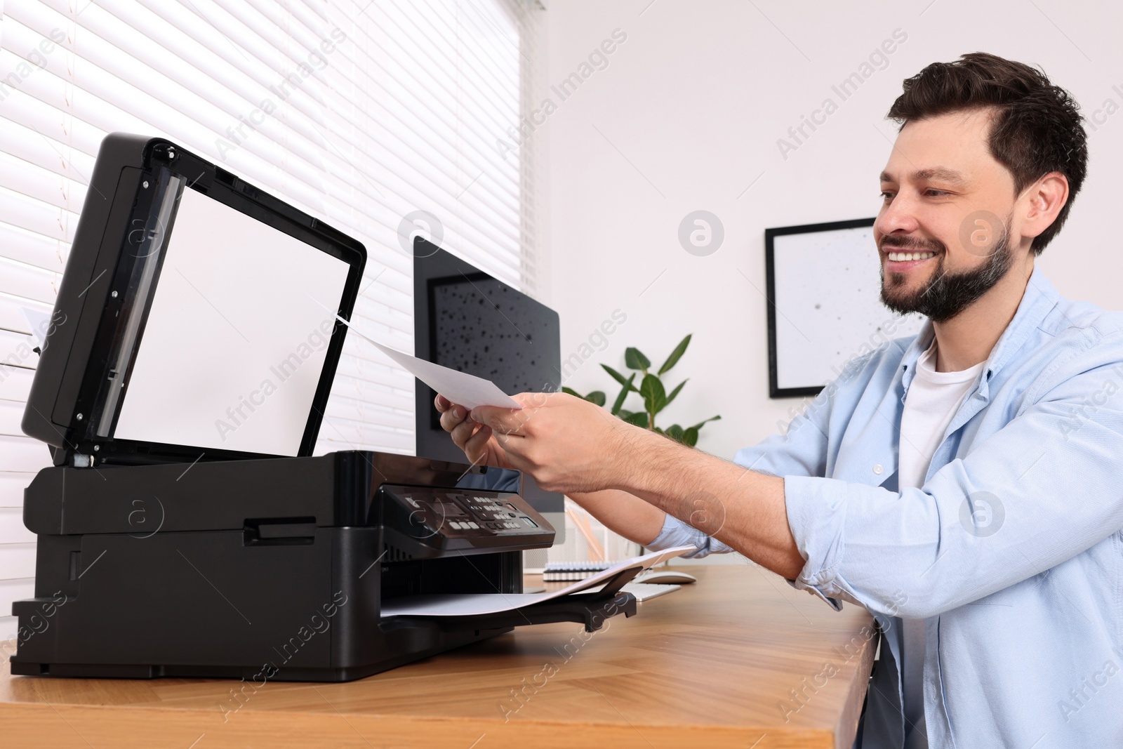 Photo of Man using modern printer at wooden table indoors