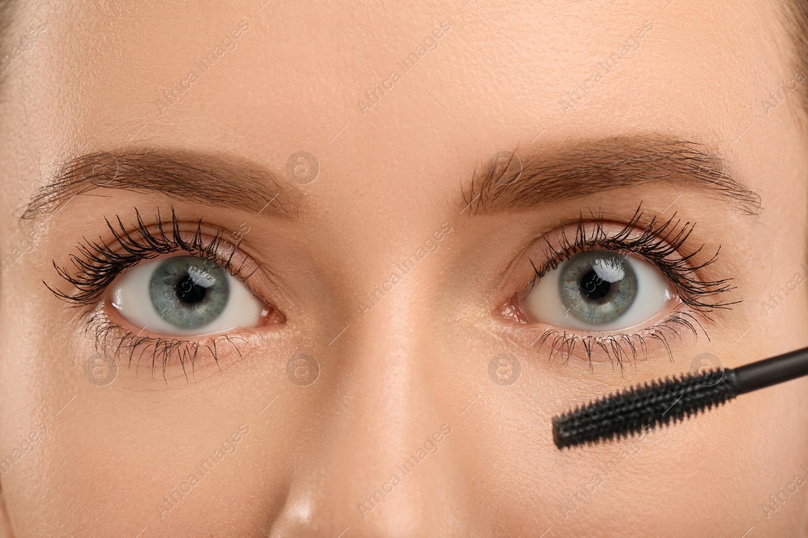 Photo of Woman applying mascara onto eyelashes, closeup view