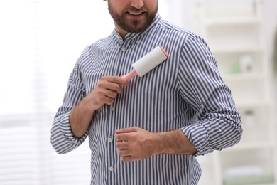 Photo of Man cleaning clothes with lint roller at home, closeup