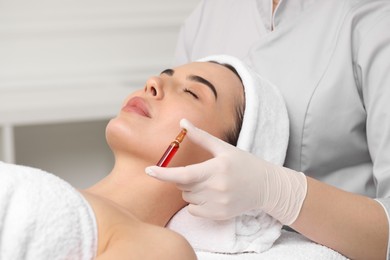 Professional cosmetologist holding skincare ampoule while working with client in clinic, closeup