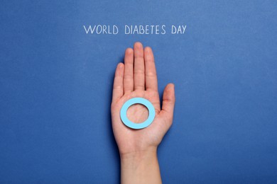 Photo of Woman holding blue paper circle near text World Diabetes Day on color background, top view