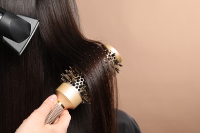 Photo of Hairdresser blow drying client's hair on beige background, closeup. Space for text