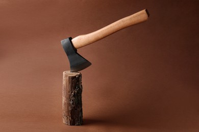 Metal ax in wooden log on brown background