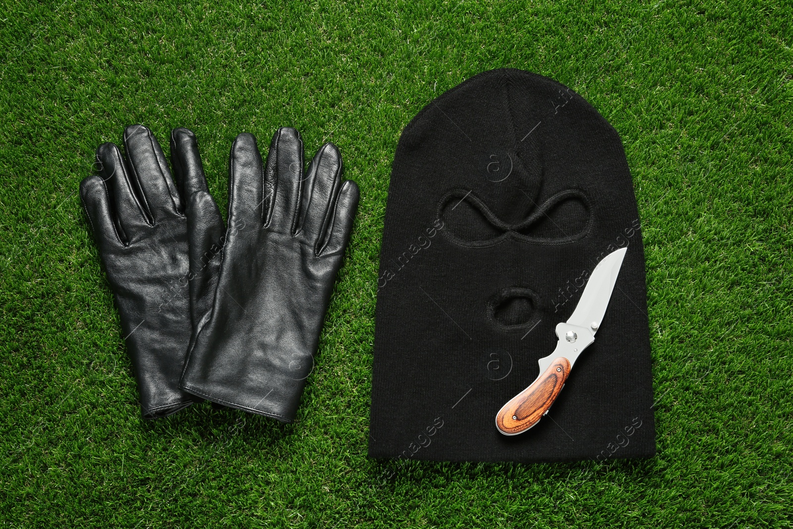 Photo of Black knitted balaclava, gloves and knife on green grass, flat lay
