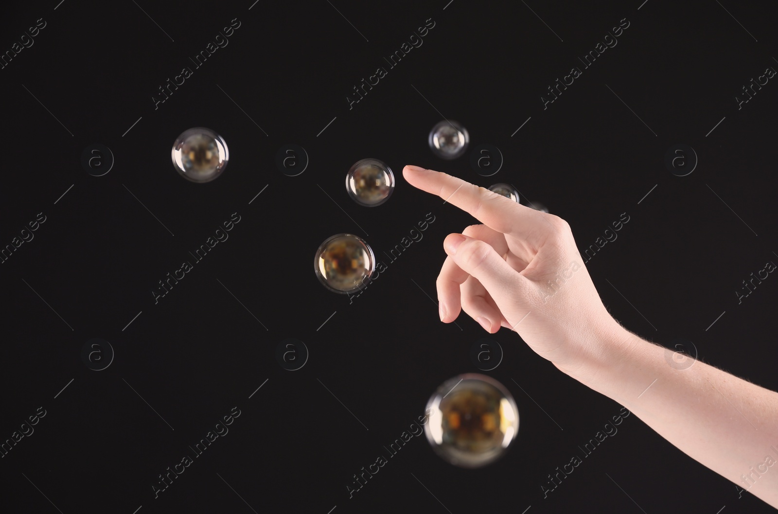 Photo of Woman popping soap bubbles on dark background, closeup