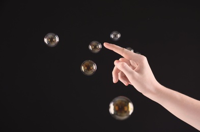 Woman popping soap bubbles on dark background, closeup