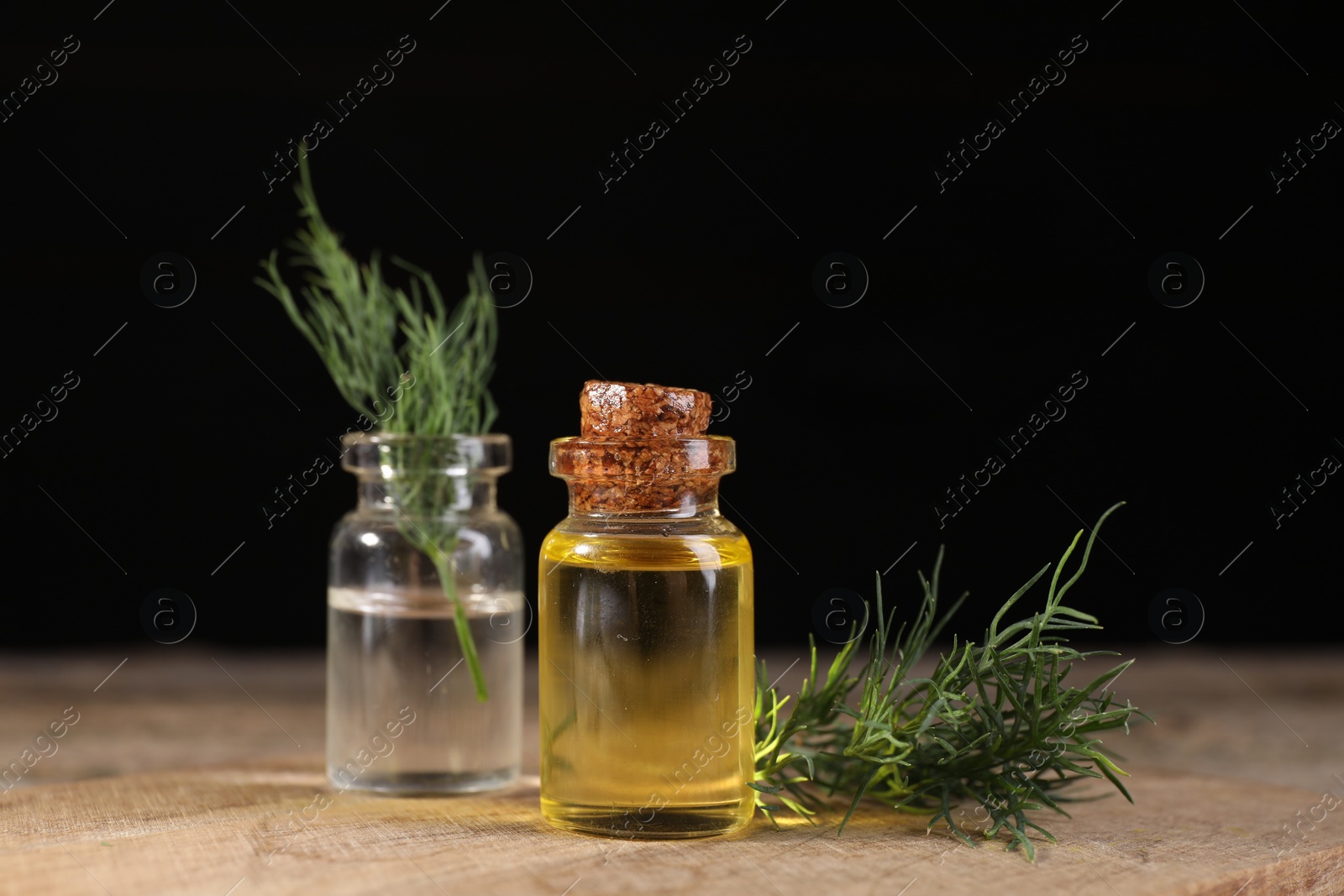 Photo of Bottles of essential oil and fresh dill on wooden table against black background