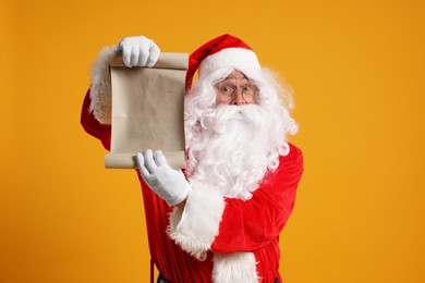 Photo of Merry Christmas. Santa Claus showing blank paper sheet on orange background