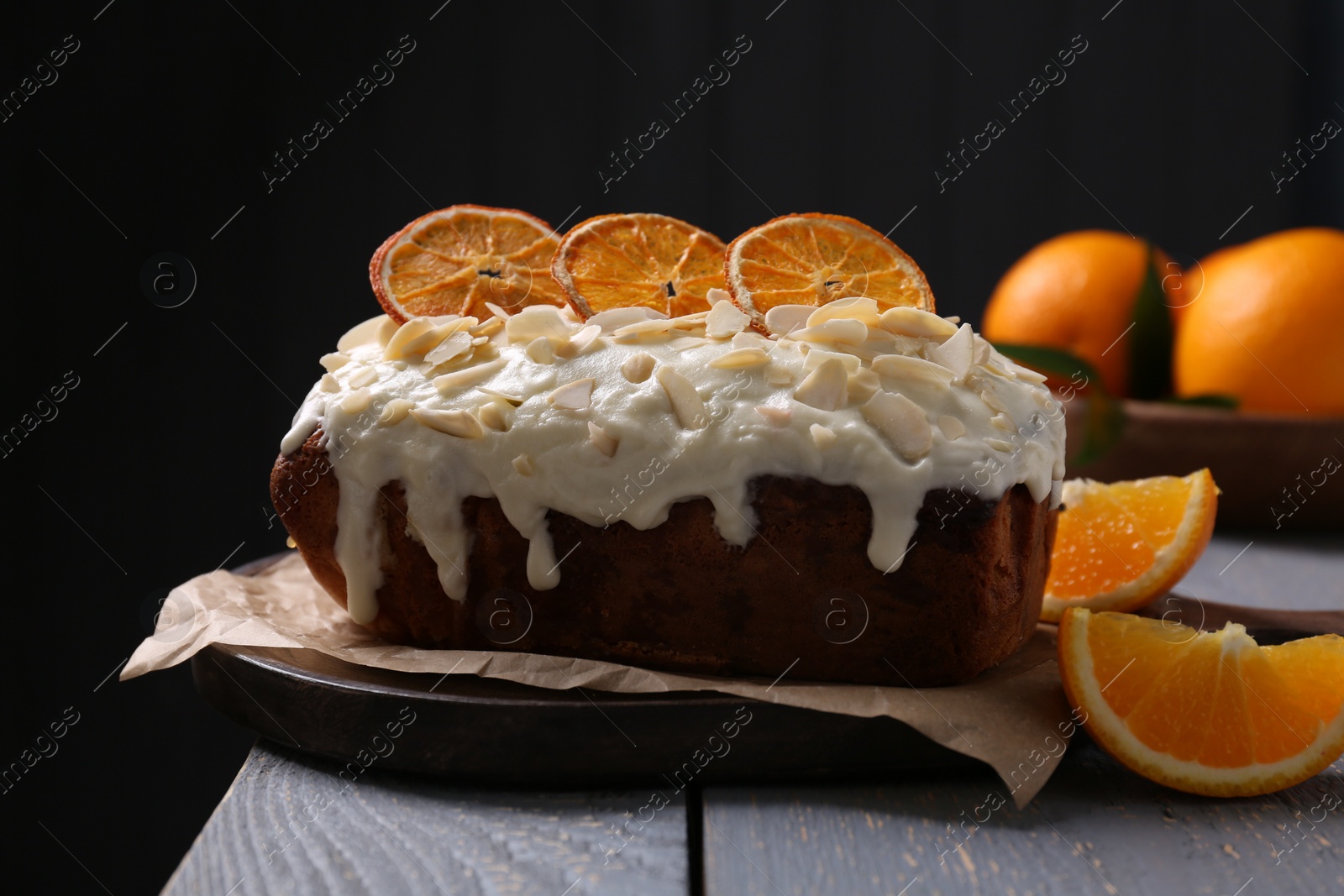 Photo of Delicious sweet cake with dry orange and almond petals on grey wooden table
