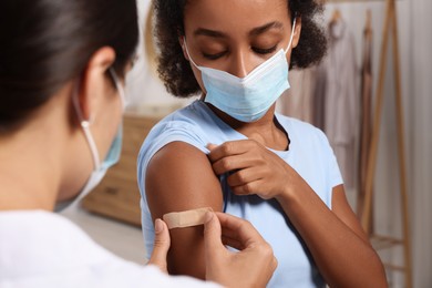 Photo of Doctor putting adhesive bandage on young woman's arm after vaccination indoors